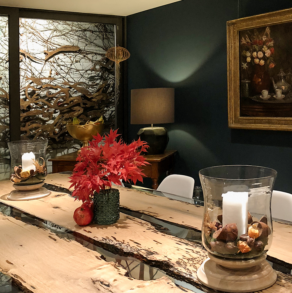 Gemütlich beleuchtetes Wohnzimmer im Herbst-Look mit warmem Kerzenlicht, Laterne, Kürbis und herbstlicher Deko auf einem Holztisch. Im Hintergrund sorgt eine Tischlampe für indirektes Licht und schafft eine einladende, stimmungsvolle Atmosphäre – perfekt für Interior- und Wohninspiration im Herbst und Winter.