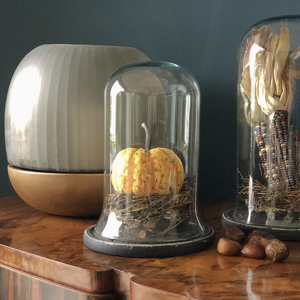 Gemütlich beleuchtetes Wohnzimmer im Herbst-Look mit warmem Kerzenlicht, Laterne, Kürbis und herbstlicher Deko auf einem Holztisch. Im Hintergrund sorgt eine Tischlampe für indirektes Licht und schafft eine einladende, stimmungsvolle Atmosphäre – perfekt für Interior- und Wohninspiration im Herbst und Winter.